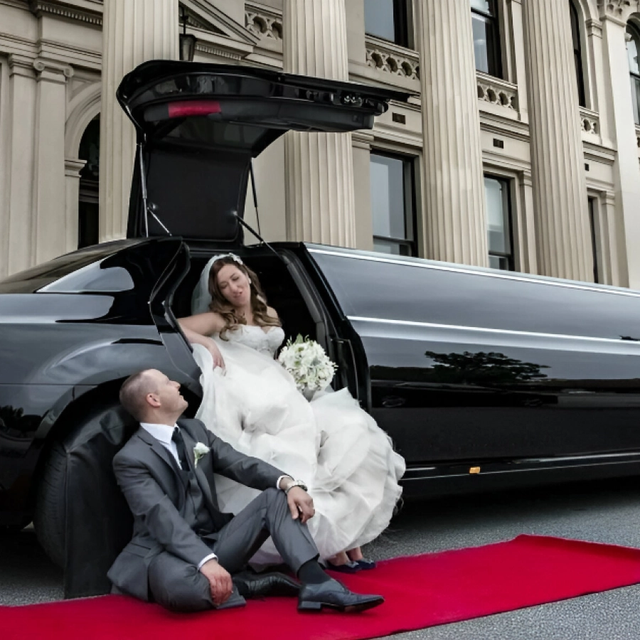 Bride and groom sitting by limousine.