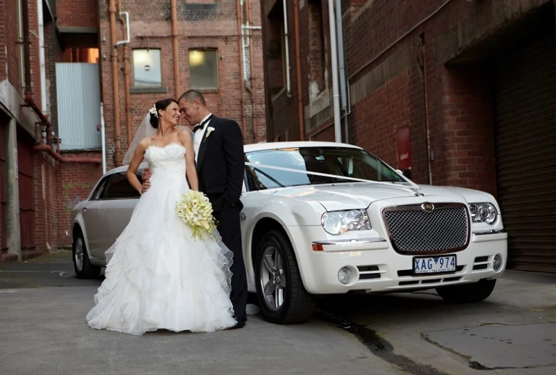 Bride and groom kissing beside white car.